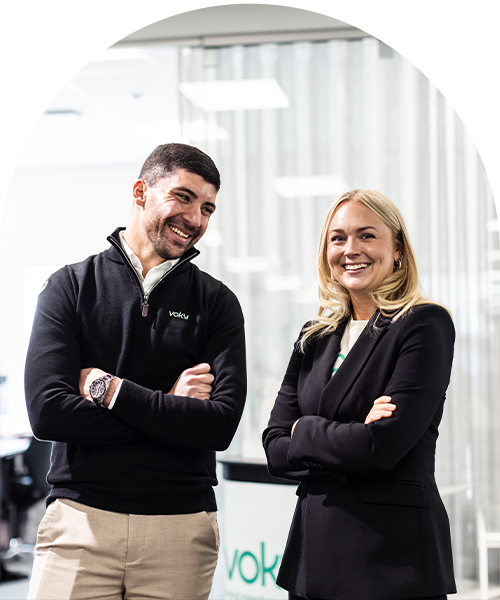 Två Voky-anställda ler med armarna i kors i en kontorsmiljö