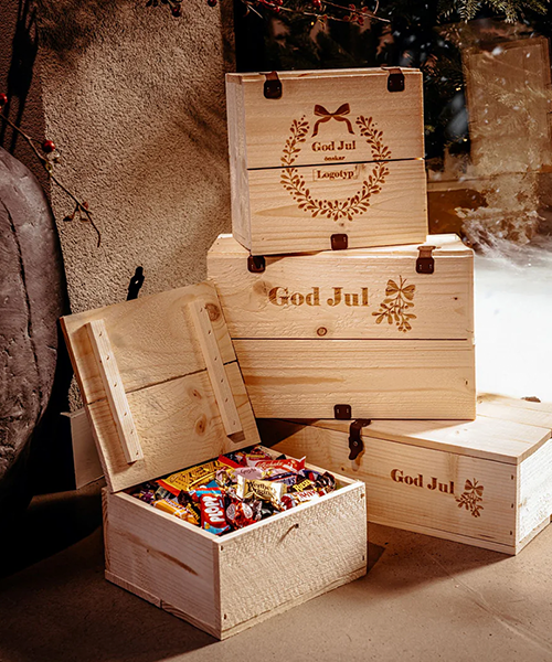 En stapel av fyra trälådor med julhälsningar och motiv. Den nedre lådan är öppen och fylld med inslaget julgodis.